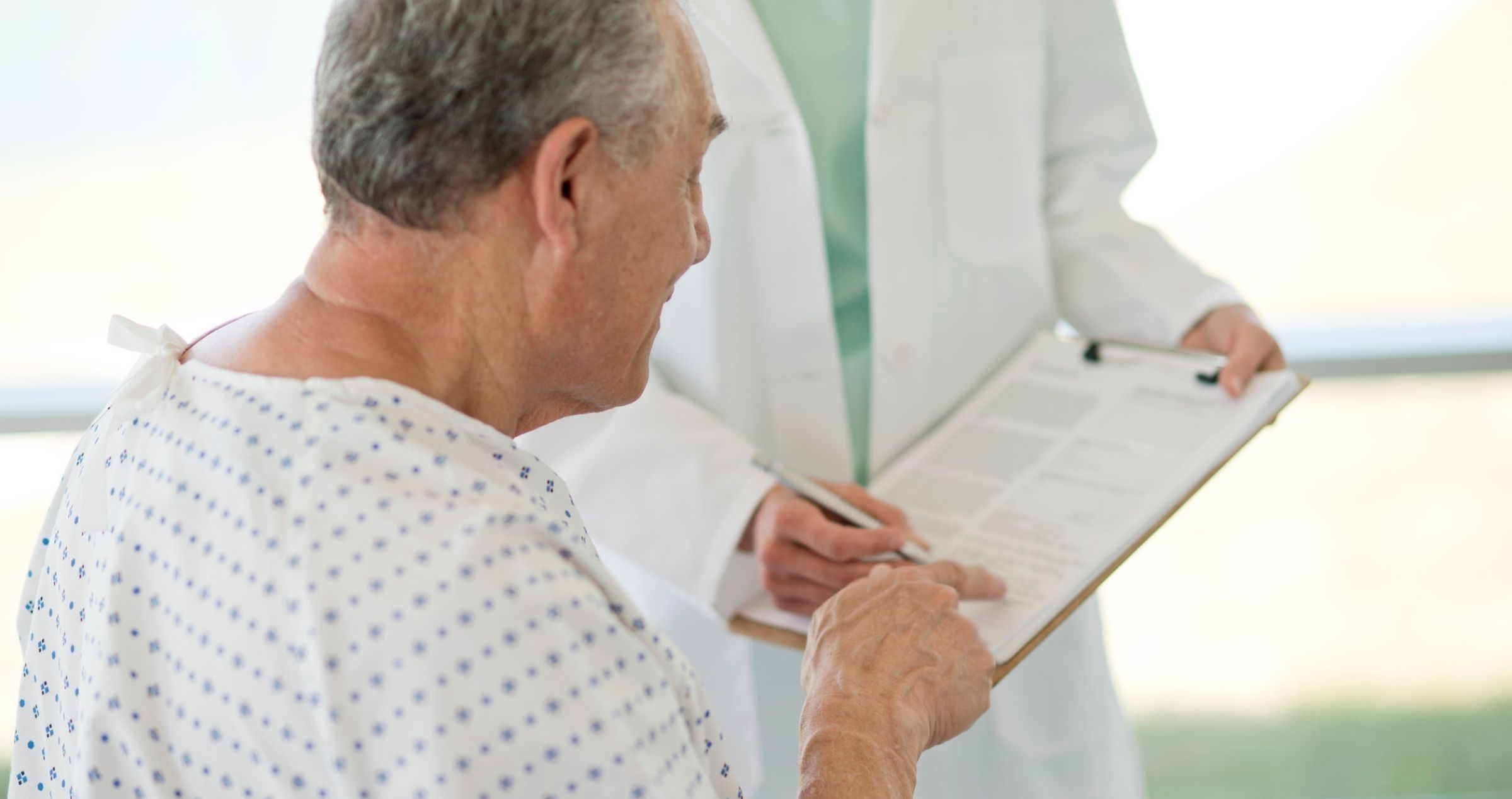 Male patient in hospital bed signing document